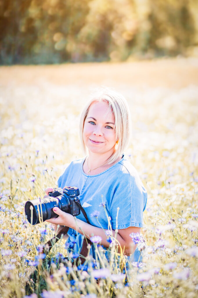 Fotograf Martina Ardbäck sitter på en äng fullt med blommor och i sin hand har hon sin Nikon systemkamera.
