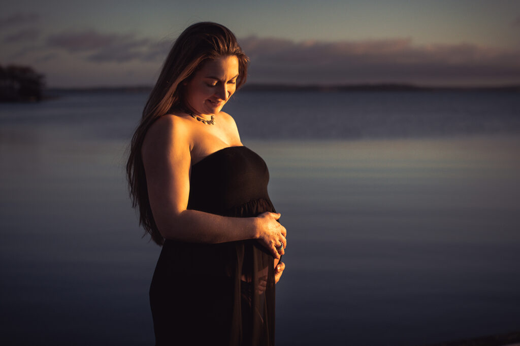 Siluett av gravid i solnedgång, Golden hour vid Mälaren, Stallarholmen, Strängnäs, Södermanland. Svart skir gravidklänning. Foto Martina Ardbäck