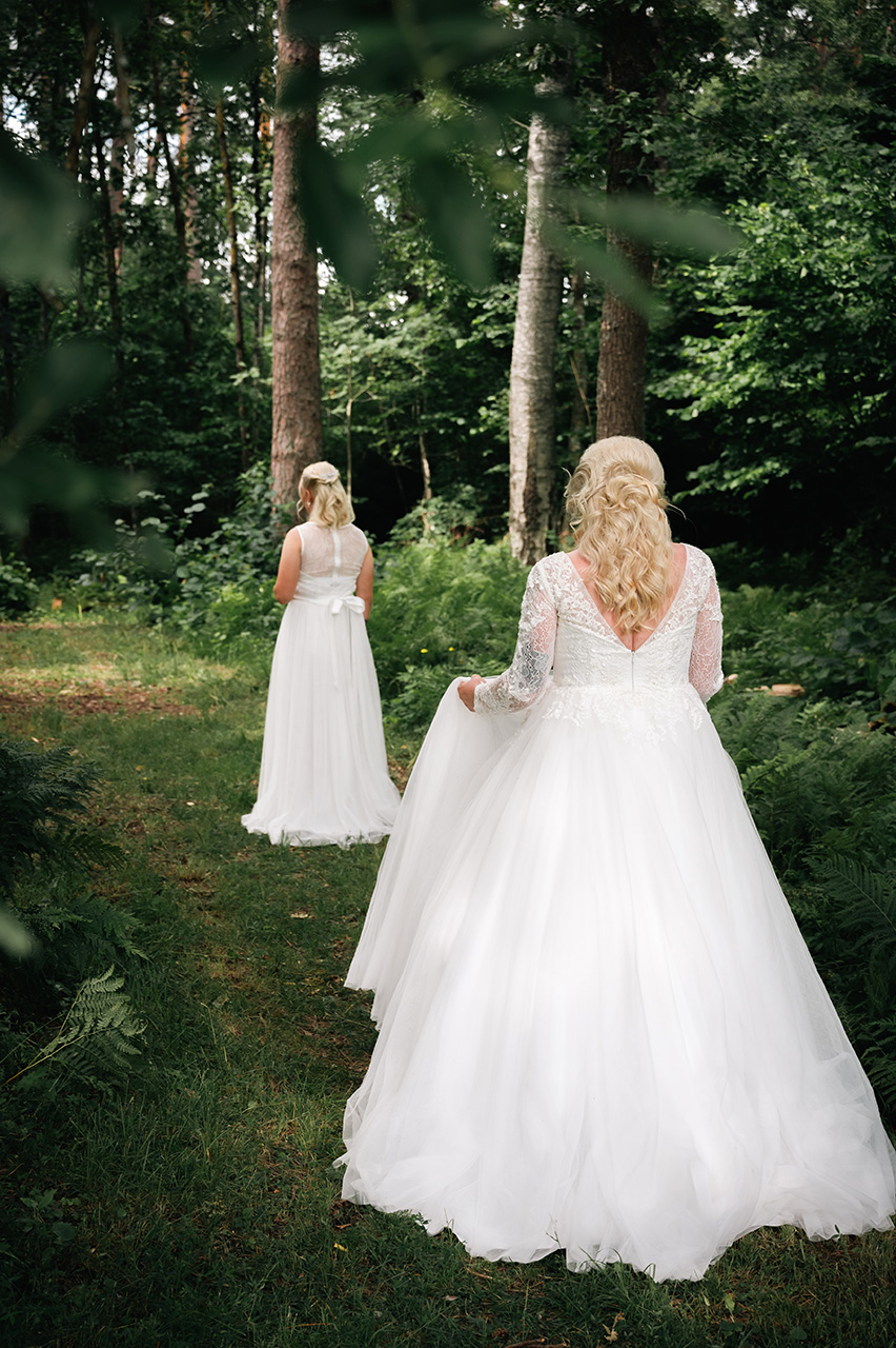First look, första gången bruden får se sin brud. Kommer gående bakifrån i skogen utanför Västerås, Västmanland där bruden väntar. Båda har vita vackra bröllopsklänningar. Foto Martina Ardbäck